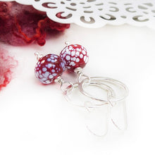 Silver earrings with red and white speckled beads on a white background