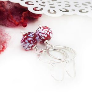 Silver earrings with red and white speckled beads on a white background