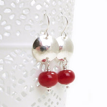 Pair of earrings with red beads and silver hammered discs on a white background
