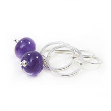 Pair of earrings with purple beads and silver loops on a white background