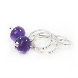 Pair of earrings with purple beads and silver loops on a white background