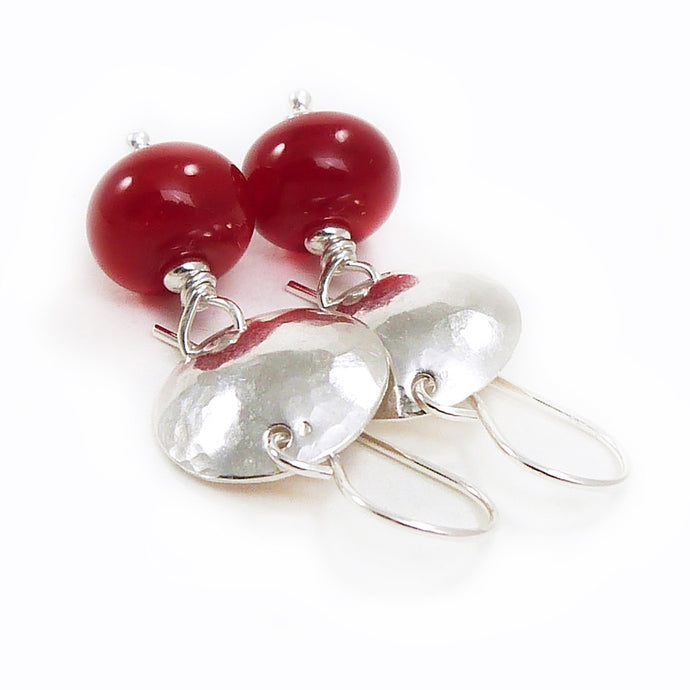 Pair of earrings with red beads and silver hammered discs on a white background