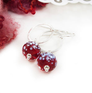 Silver earrings with red and white speckled beads on a white background