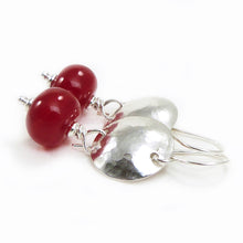 Pair of earrings with red beads and silver hammered discs on a white background