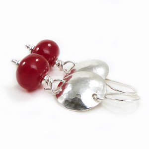 Pair of earrings with red beads and silver hammered discs on a white background