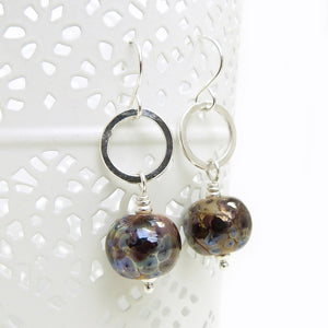 Pair of earrings with round brown beads and silver loops on a white background