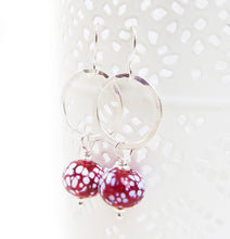 Silver earrings with red and white speckled beads on a white background