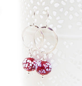 Silver earrings with red and white speckled beads on a white background