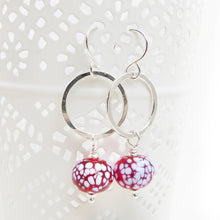 Silver earrings with red and white speckled beads on a white background