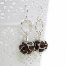 Pair of earrings with leopard print beads and silver hooks on a white background