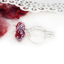Silver earrings with red and white speckled beads on a white background
