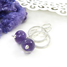Purple glass beads with silver rings on a white surface