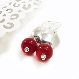 Pair of earrings with red beads and silver hammered discs on a white background