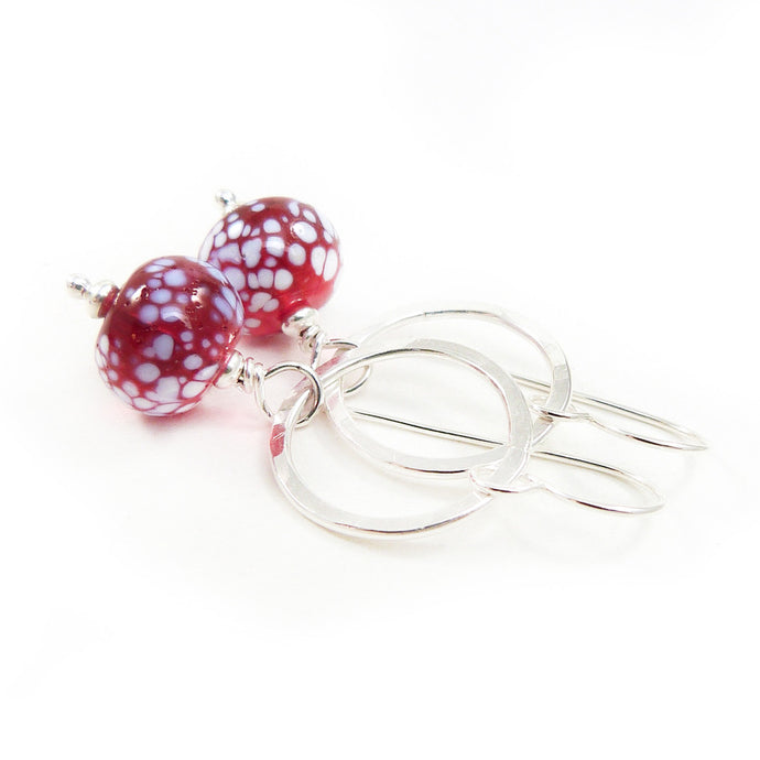 Silver earrings with red and white speckled beads on a white background