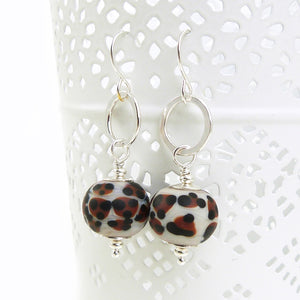 Pair of earrings with leopard print beads and silver hooks on a white background