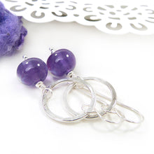 Silver hoop earrings with purple beads on a white lace background