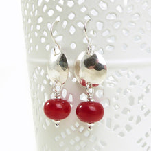 Pair of earrings with red beads and silver hammered discs on a white background