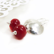 Pair of earrings with red beads and silver hammered discs on a white background